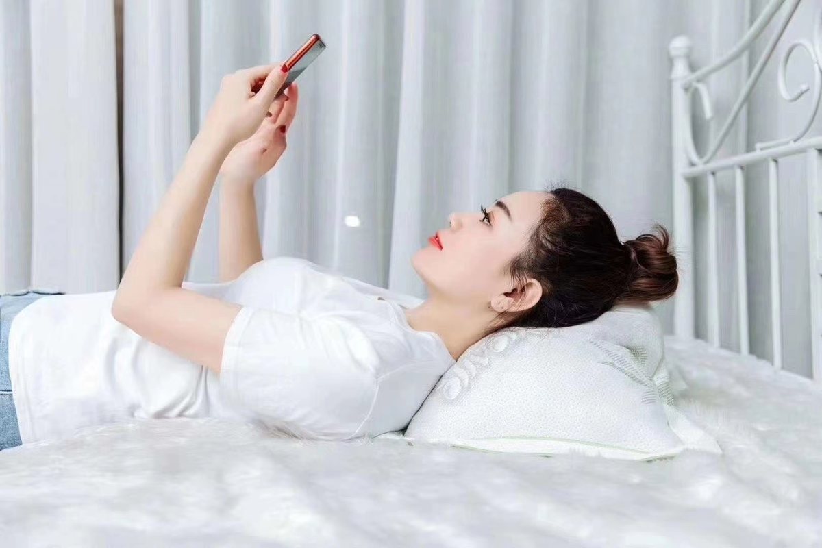 Reclining in bed with the Zhuyun pillow molded under the neck while scrolling a phone